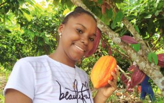 mujer sonriendo, sosteniendo en su mano un fruto del árbol de cacao