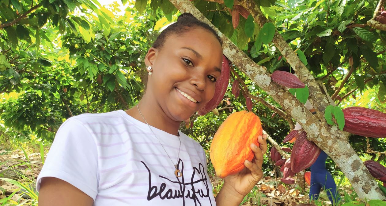 mujer sonriendo, sosteniendo en su mano un fruto del árbol de cacao
